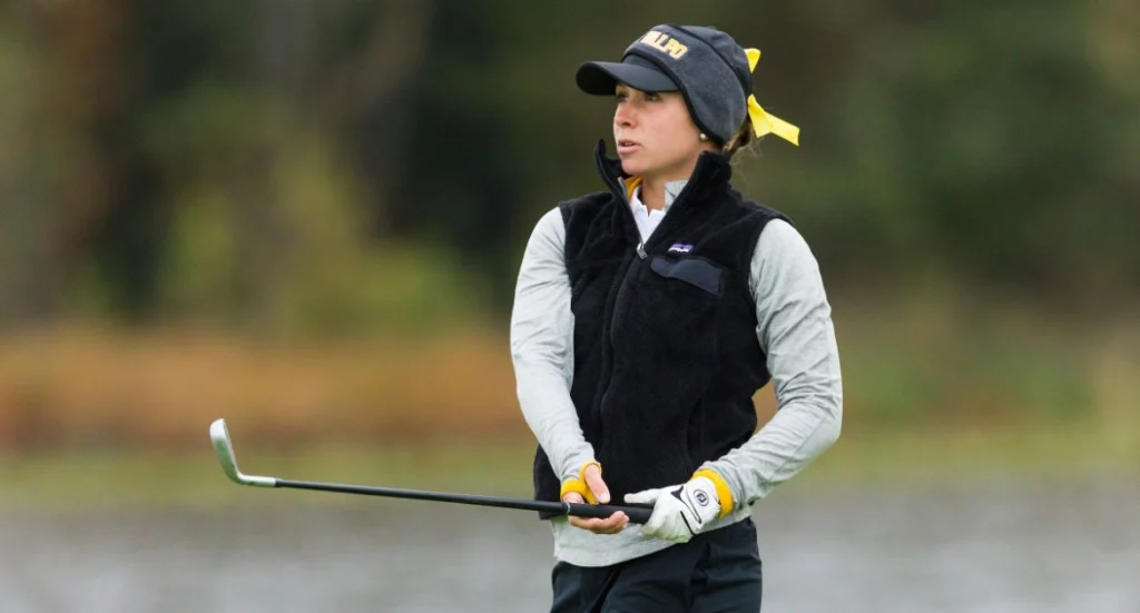 A Valpo Student-Athlete with a yellow ribbon in her hair watches her shot on the golf course.