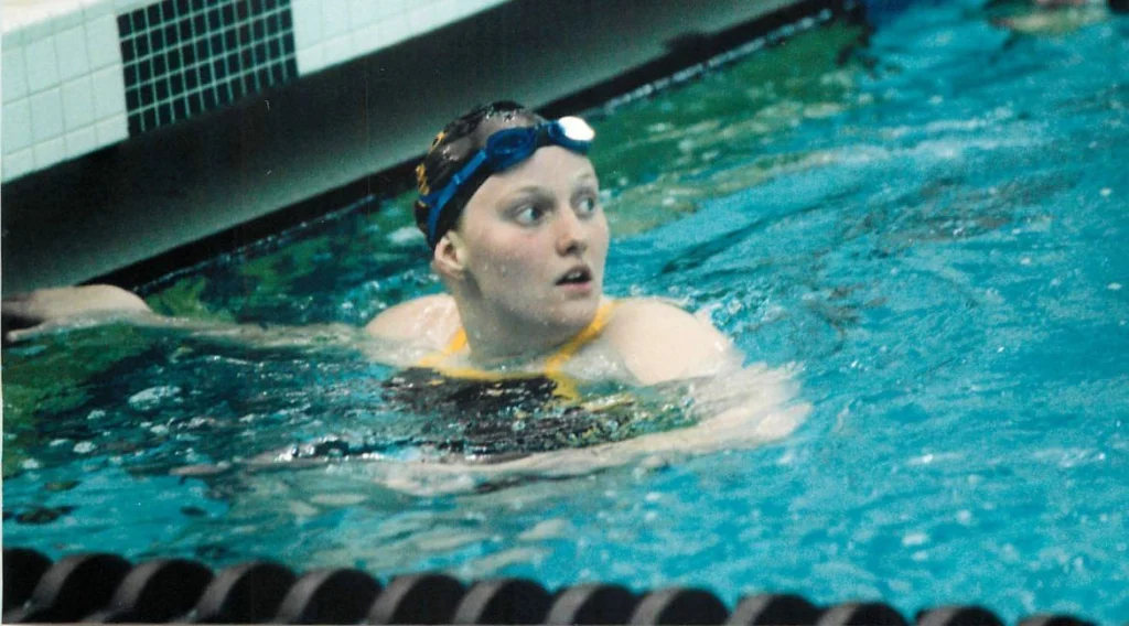 A Valpo student-athlete in goggles holds the pool edge, looking to the side, during a swim meet.