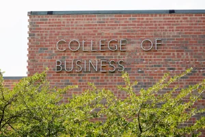Red brick building with "College of Business" sign and green trees in the foreground, highlighting its renowned business accreditation.