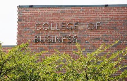 Red brick building with "College of Business" sign and green trees in the foreground, highlighting its renowned business accreditation.