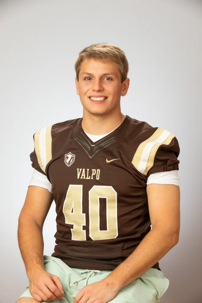 Smiling young man in a Valpo football jersey with number 40, seated against a plain light background, radiates singular focus and determination.