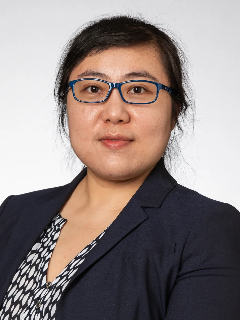 Woman with glasses in a navy blazer and patterned blouse, posing against a plain light background—her confident style reflects an enthusiasm for collaboration and collaborative learning.