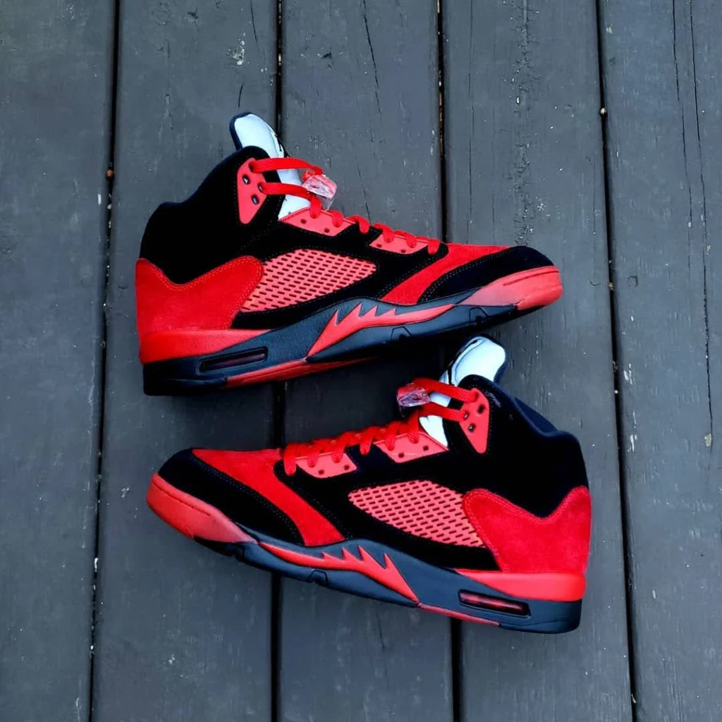 A pair of red and black Air Jordan sneakers, showcasing custom shoe customization, placed on a dark wooden floor.