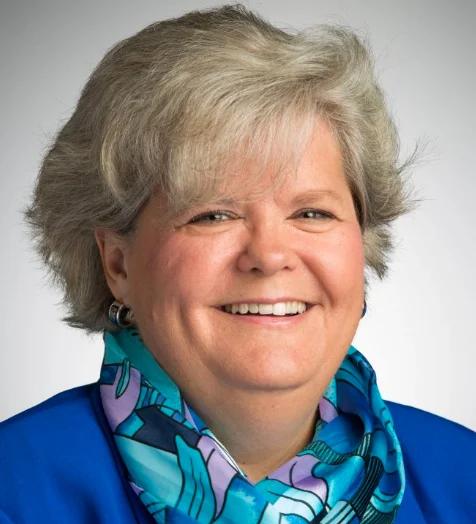 Smiling older woman with short gray hair, wearing a blue jacket and patterned scarf, recognized by Valparaiso University for her Research and Creative Work.