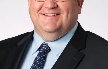 Smiling man wearing glasses, a black suit, blue shirt, and patterned tie, posing against a light background—Doug Tougaw of the College of Engineering exemplifies engineering leadership.
