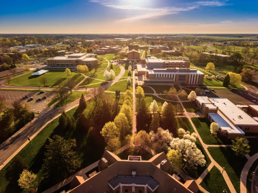 Aerial view of a university campus with green lawns, trees, and academic buildings at sunrise—discover inspiring ways to visit Valpo and experience its beauty.