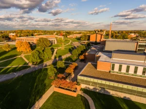 Aerial view of a college campus with green lawns, trees, and modern brick buildings under a partly cloudy sky—come visit Valpo and experience its vibrant atmosphere.