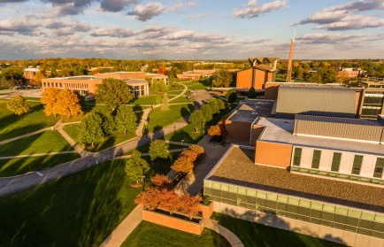 Aerial view of a college campus with green lawns, trees, and modern brick buildings under a partly cloudy sky—come visit Valpo and experience its vibrant atmosphere.