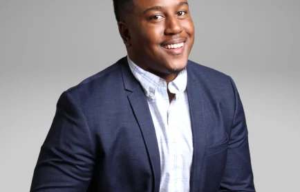 Smiling Valpo alumnus in a blue suit jacket and white shirt poses against a plain grey background, ready to embrace new challenges.