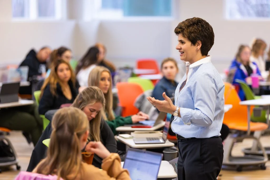 A teacher with a passion for education speaks to students seated at desks in a bright, modern classroom, embodying the dedication seen in Valpo professors.