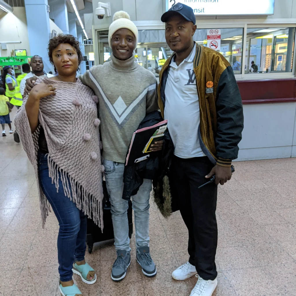 With determination, three people pose together in an indoor public space, smiling at the camera. Charles Smith stands among them, reflecting a spirit of innovation.