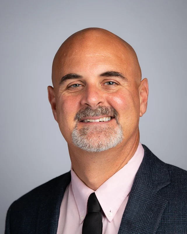 Bald man with a goatee in a suit, pink shirt, and black tie smiling at the camera as one of the new faculty for the Master of Social Work program at Valparaiso University.