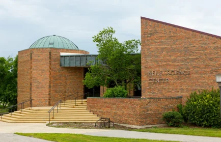 Brick building with dome roof, entrance steps, and sign reading "Neils Science Center" on the wall.