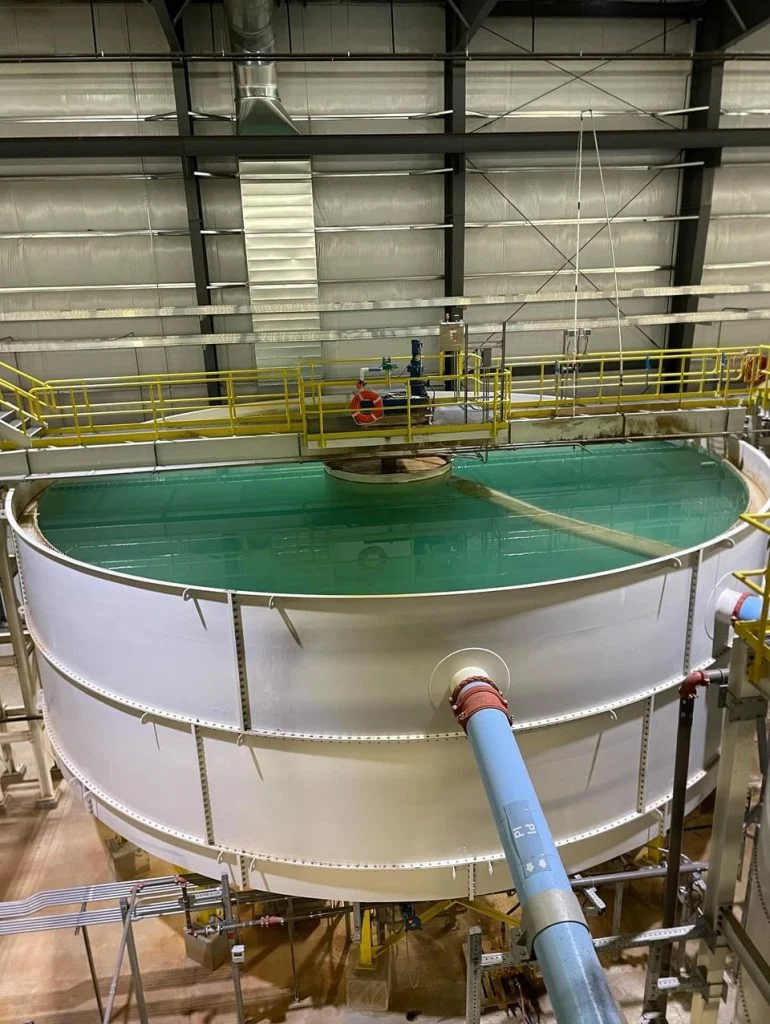 Large indoor tank filled with greenish liquid, surrounded by yellow railings and industrial equipment—an example of Outcomes in Action in an industrial setting.