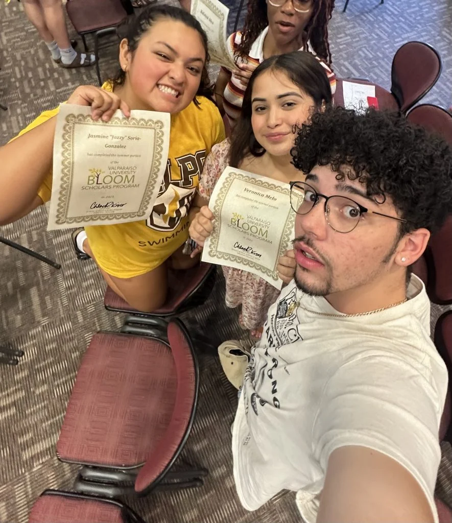 Three smiling people, including Jazzy Soria-Gonzalez, hold certificates and pose for a selfie in a room with rows of red chairs, celebrating an eventful first year.