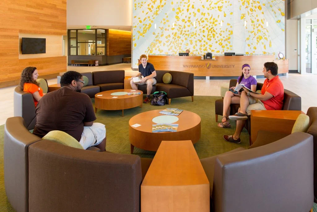 Five students sit and talk in a modern Valpo campus lounge area with round tables and a bright mural behind them, reflecting the welcoming vibe of one of the region's most transfer-friendly schools.