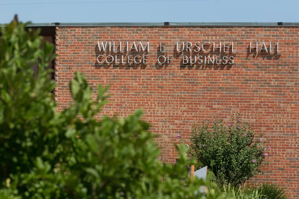 Brick building with sign reading "William E. Urschel Hall College of Business" at Valparaiso University, partially obscured by greenery—home to one of the Princeton Review’s Top 50 Programs.