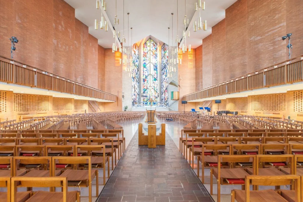 Modern church interior with wooden chairs, high ceiling, and a large colorful stained glass window at the front—a beautiful setting for celebrating Lutheran Summer Music and honoring a rich liturgical legacy.