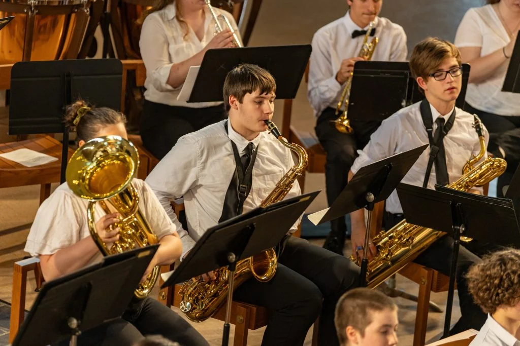 Students in white shirts play saxophones and brass instruments in a vibrant Lutheran Summer Music school band performance.