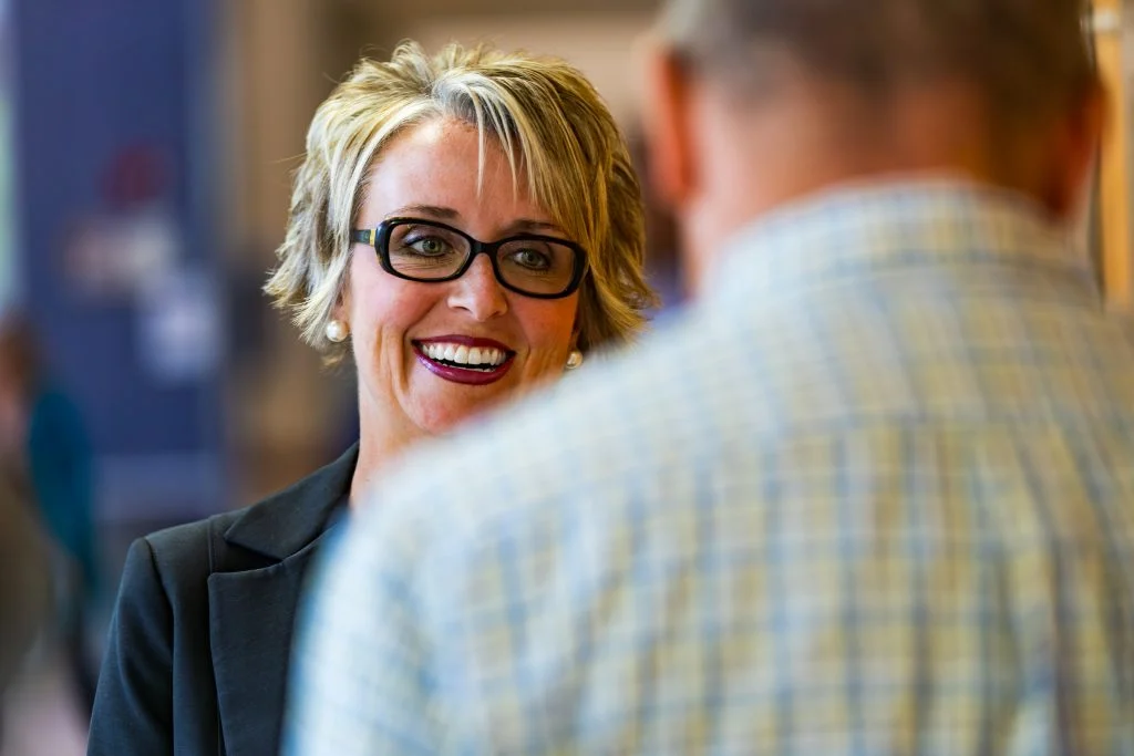 Smiling woman with glasses, Nadia Paul, talks to a man in a plaid shirt indoors, reflecting on their journey toward Bright Outcomes and a Balanced Life.