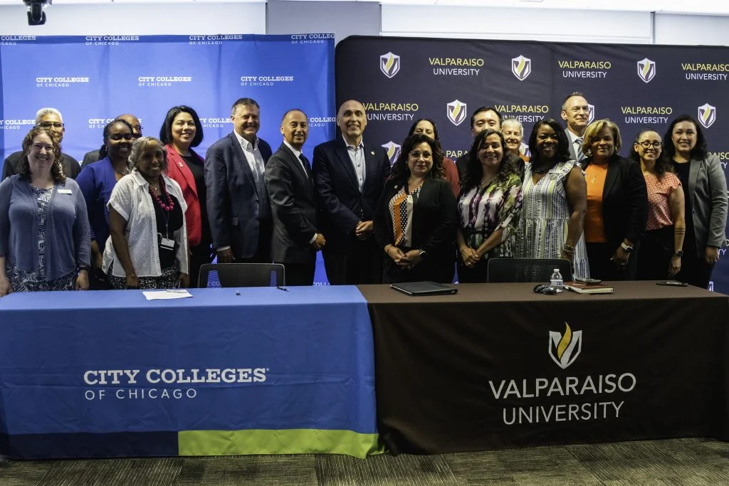A group of people pose by tables with City Colleges of Chicago and Valparaiso University banners in the background, highlighting a guaranteed admission partnership between the two institutions.