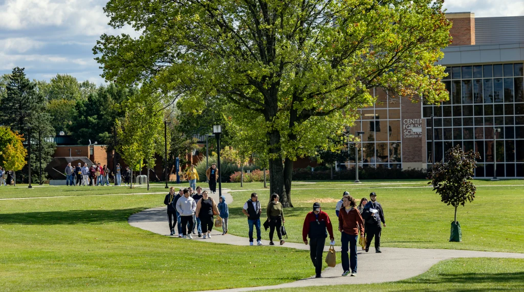 Students walk along a campus pathway lined with trees and green lawns near a modern academic building at Valpo, known for welcoming transfer students.