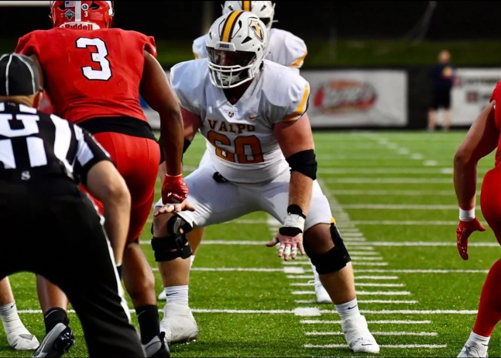 Valpo Football’s Tyler Eberhart, known for his servant-leadership, faces off against players in red on the field during an intense game.