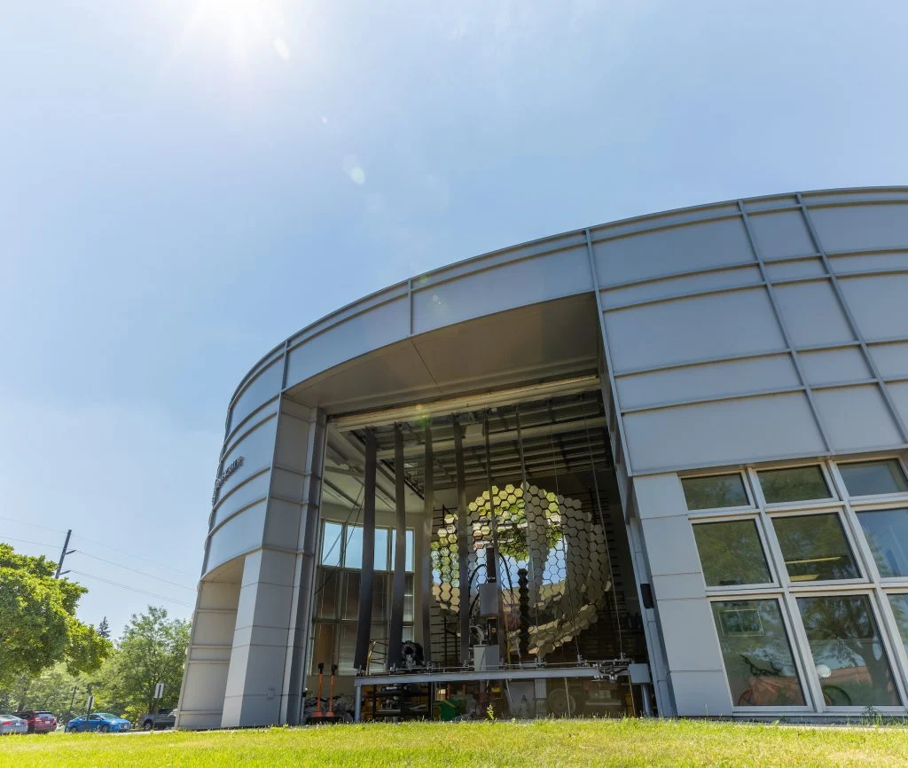 A modern glass building at Valparaiso University, featuring a large circular structure inside, is seen from a grassy lawn on a sunny day.
