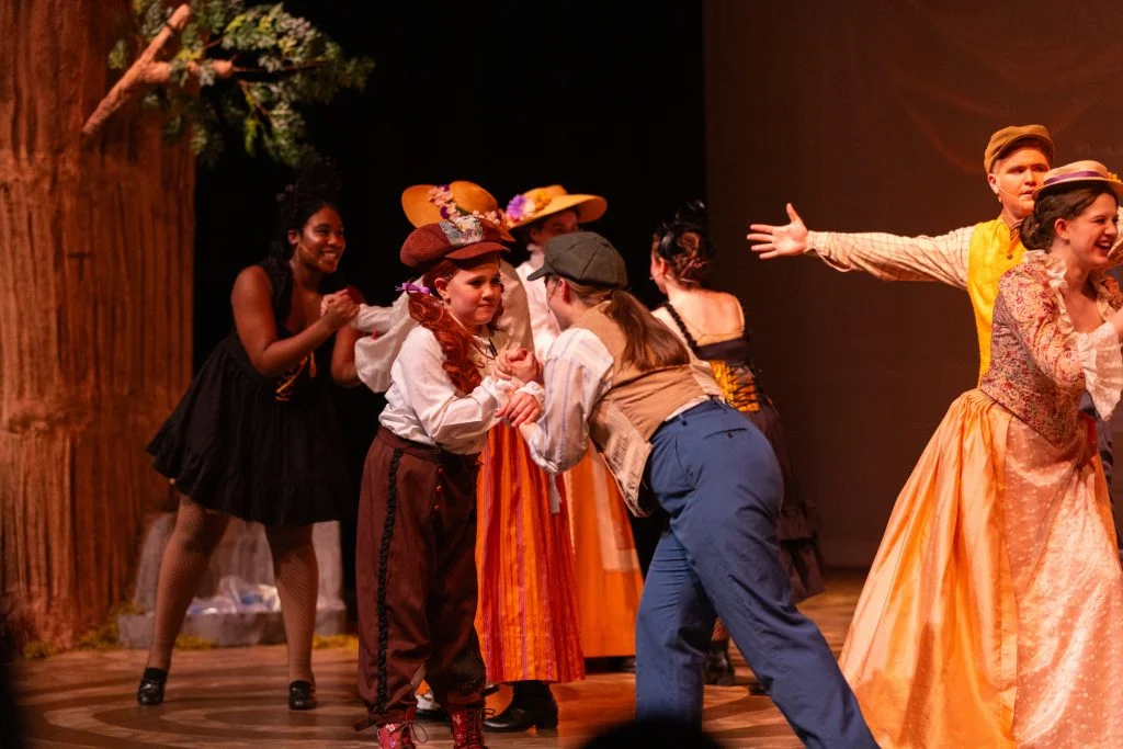 Actors in colorful costumes perform an energetic scene on stage with a forest backdrop, showcasing the vibrant talent often seen at Valparaiso University shows.