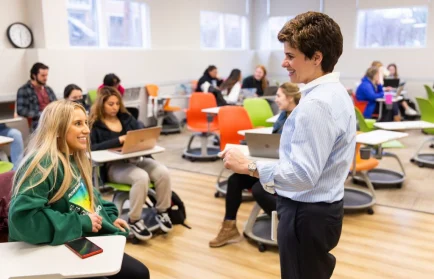 A teacher talks to a transfer student in a brightly lit Valpo classroom, where students shine as they use laptops at their desks.