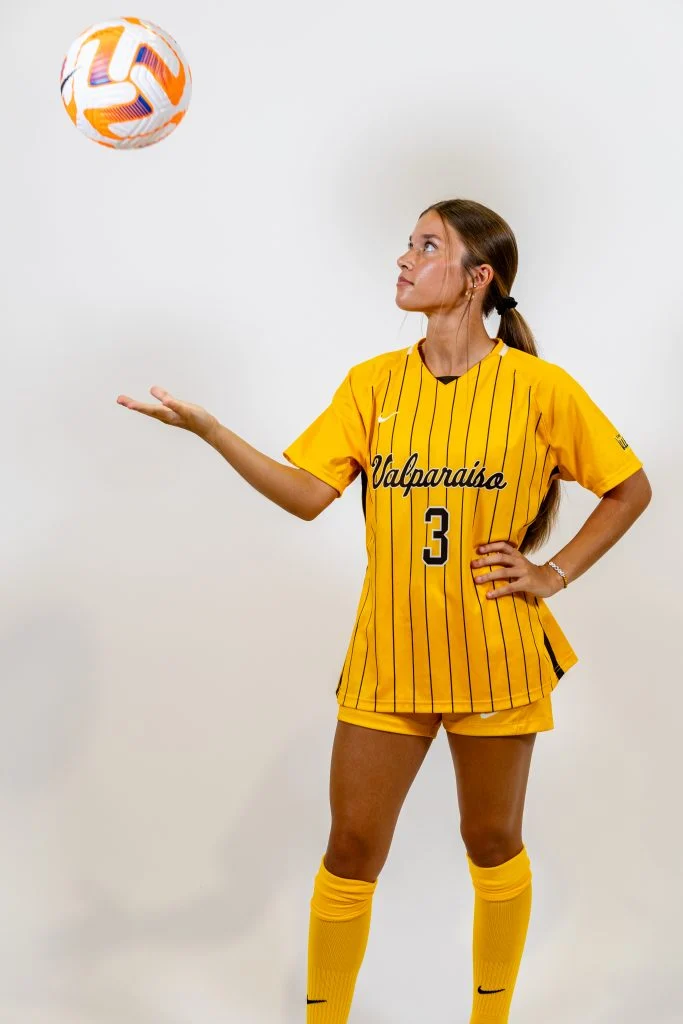 Soccer player Sam Gountounas in a yellow Valparaiso uniform tosses a ball with one hand, looking up at it—a moment that reflects the same compassion found in pediatric nursing.