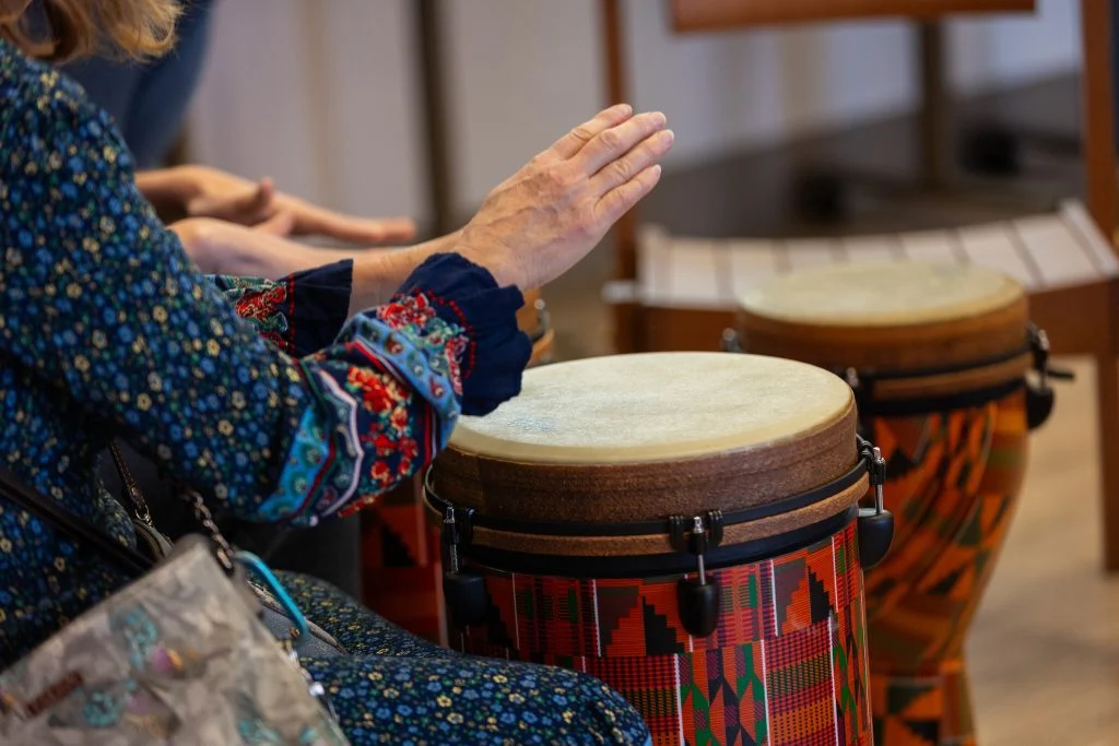 A graduate from Valparaiso University in a patterned shirt plays a colorful drum with their hand, another drum beside them, showcasing the power of music therapy.