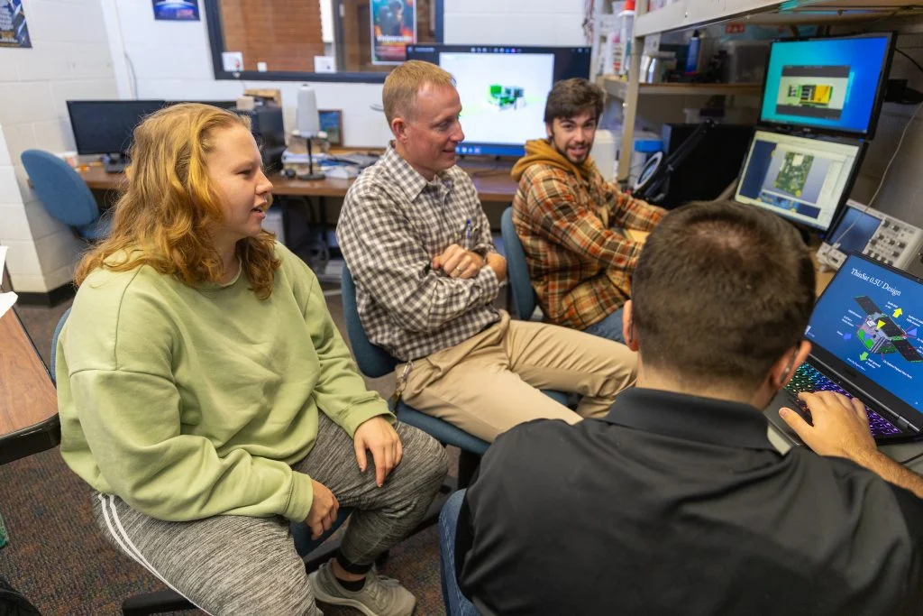Four people sit in a computer lab at Valparaiso University, discussing ideas for their undergraduate satellite project as part of the Dream Big collaboration in a relaxed, collaborative setting.