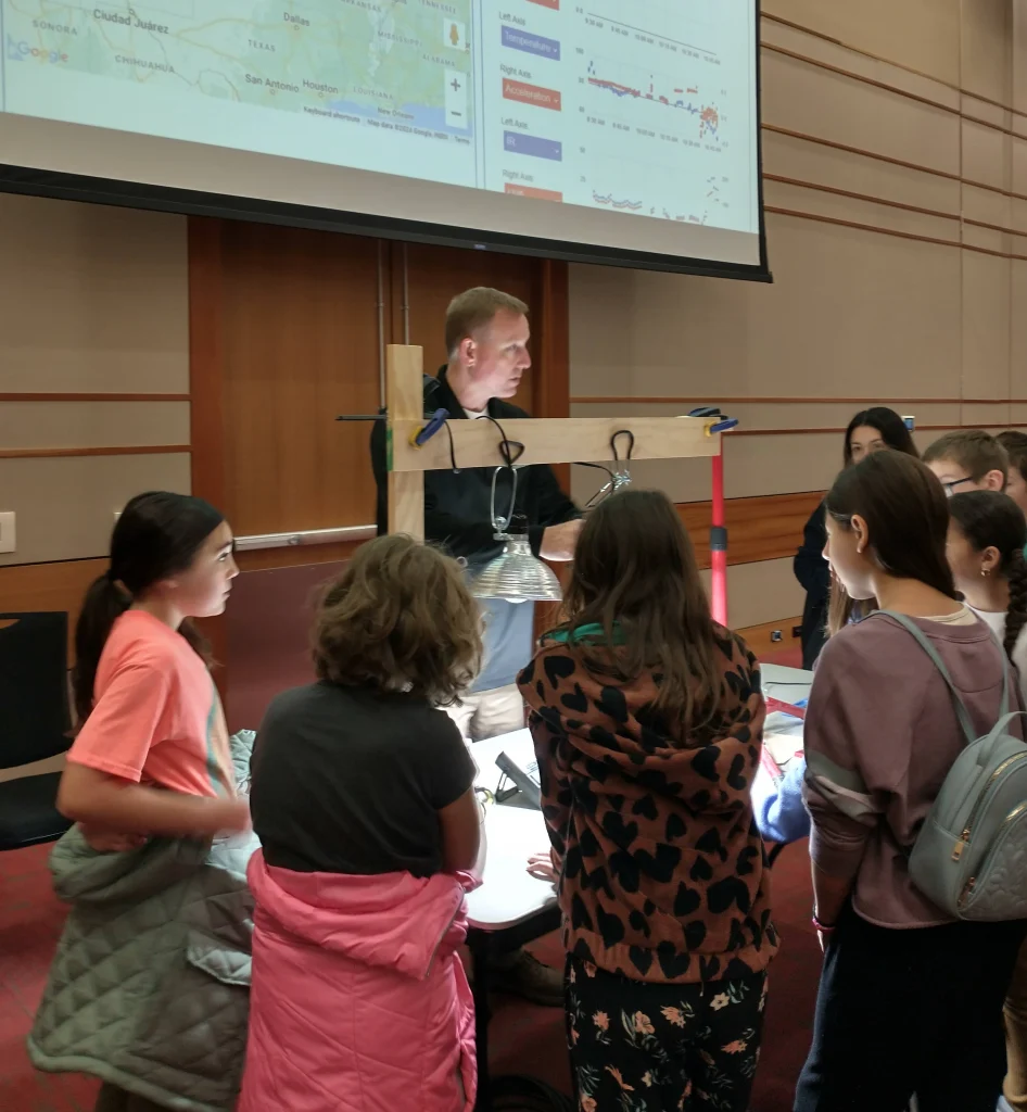 A group of Valparaiso University students gathers around a science demonstration with lights, led by an instructor in a classroom—part of their satellite team’s high-altitude balloon project.