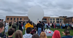 A large group gathers outside as the Valparaiso University satellite team prepares to launch a big white high-altitude balloon.