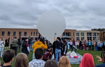 A large group gathers outside as the Valparaiso University satellite team prepares to launch a big white high-altitude balloon.