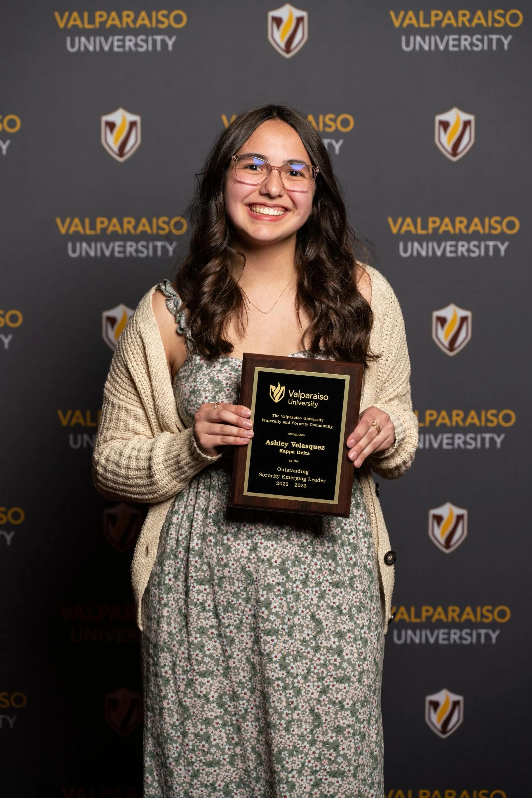 Smiling woman, Ashley Velasquez, holds an award plaque in front of a Valparaiso University backdrop, celebrating her achievements in Bioengineering.