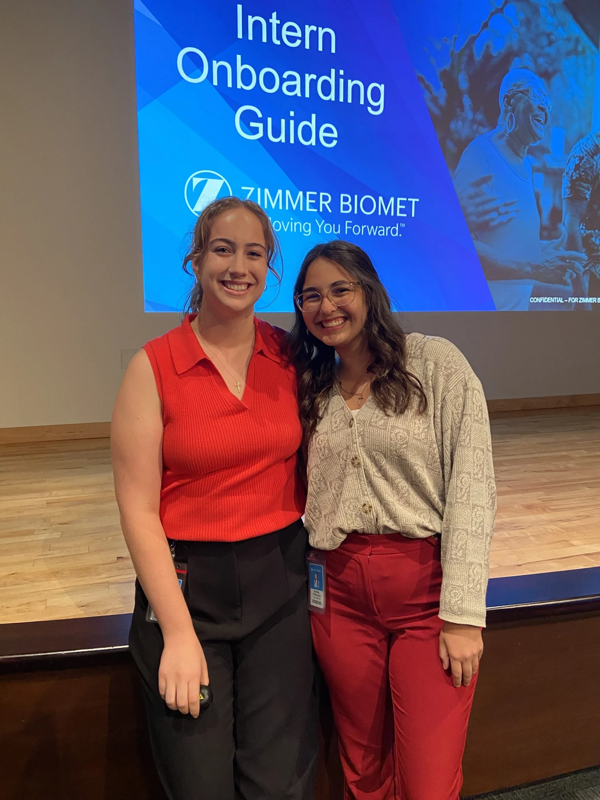 Two smiling women stand together in front of a screen displaying “Intern Onboarding Guide” at Zimmer Biomet, where Ashley Velasquez shares her passion for Bioengineering.