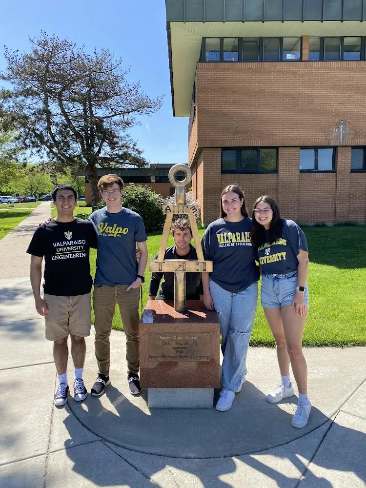 Five smiling students pose around an anchor statue on a sunny day, wearing Valparaiso University shirts and celebrating their passion for bioengineering and faith.