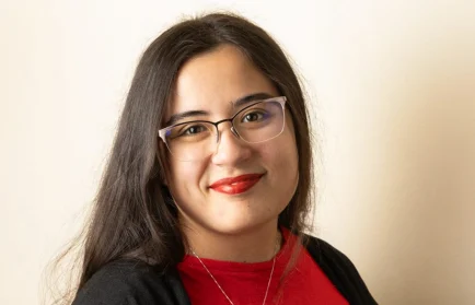 Woman with long dark hair, glasses, and red lipstick smiles, wearing a red shirt and black cardigan; a Valparaiso University graduate passionate about music therapy.