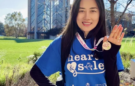 Woman in a "heart & sole" shirt and "COACH" badge, smiling outdoors and holding up a medal—celebrating as she embodies Beacon’s Reflection.