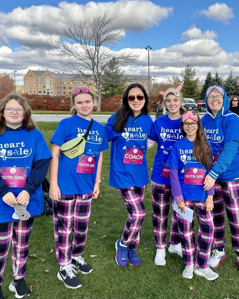 Six people in matching blue "Heart & Sole" shirts and plaid pants pose together outdoors on a grassy field, embodying the spirit of Beacon’s Reflection.
