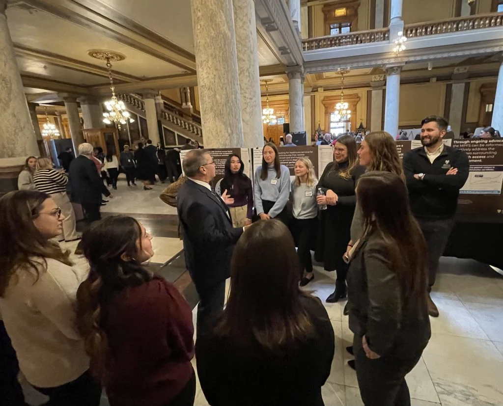 A group of occupational therapy students stand in a circle talking at an indoor event in a large, ornate building.