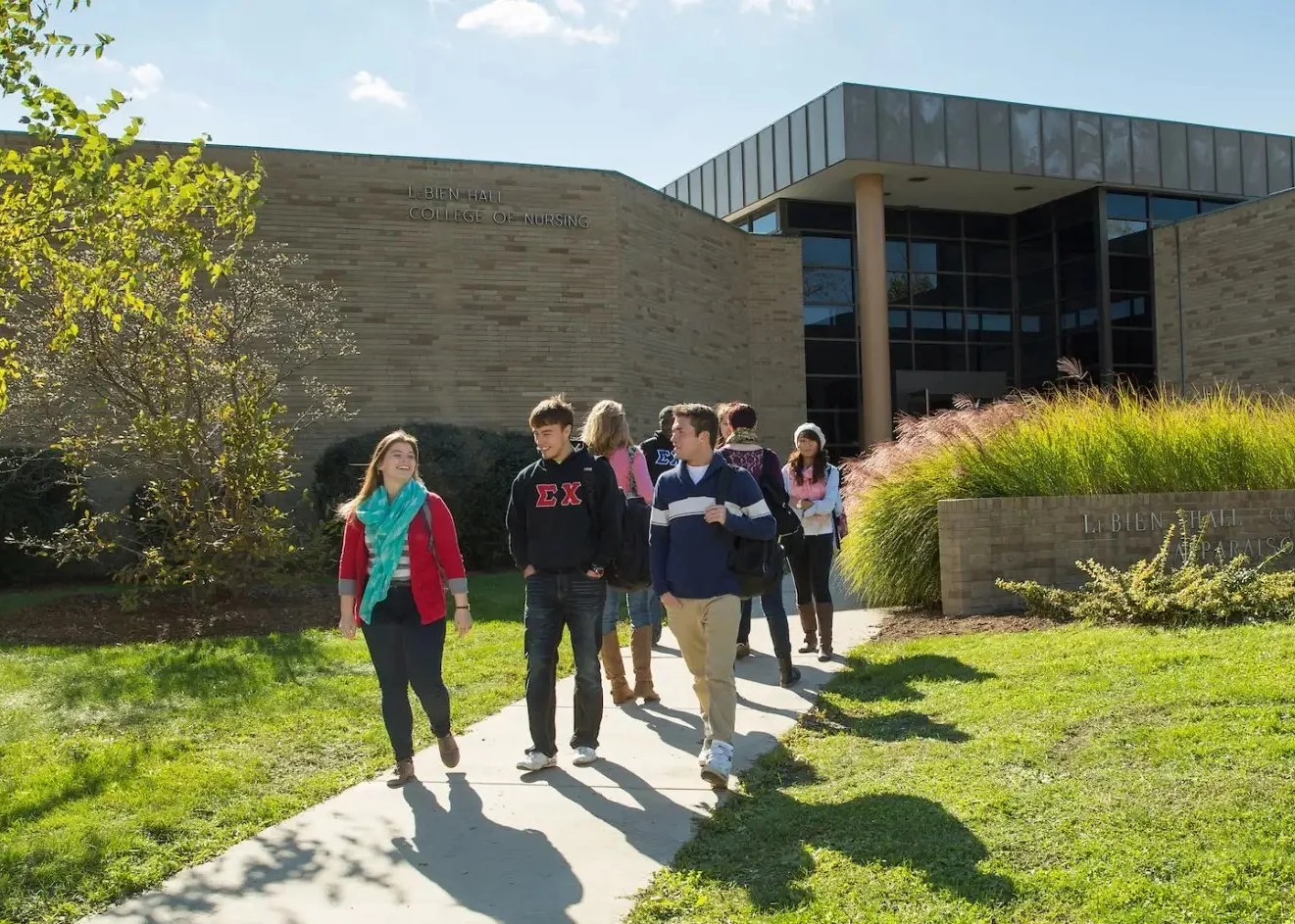 A group of college students, including those in the Physician Assistant Masters program, walk on a path outside a modern campus building on a sunny day.
