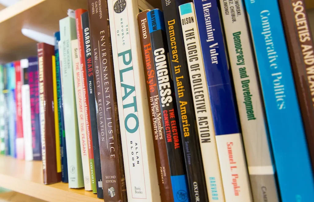 A bookshelf filled with academic books, including titles on Plato, Congress, democracy, and politics.