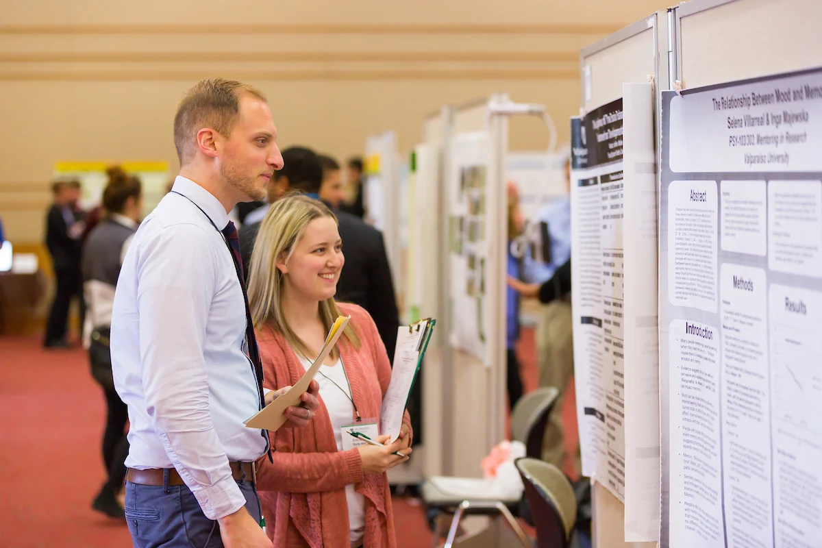 Two people with clipboards read a scientific poster at the Symposium on Undergraduate Research and Creative Expression.