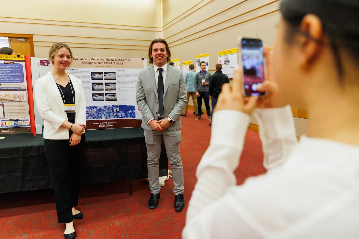 Two people pose by a research poster while another captures the moment on a smartphone, celebrating the importance of sharing your research at a conference.