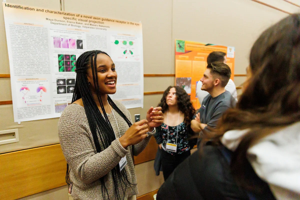 A woman presents her scientific poster to a small group at the Symposium on Undergraduate Research and Creative Expression.