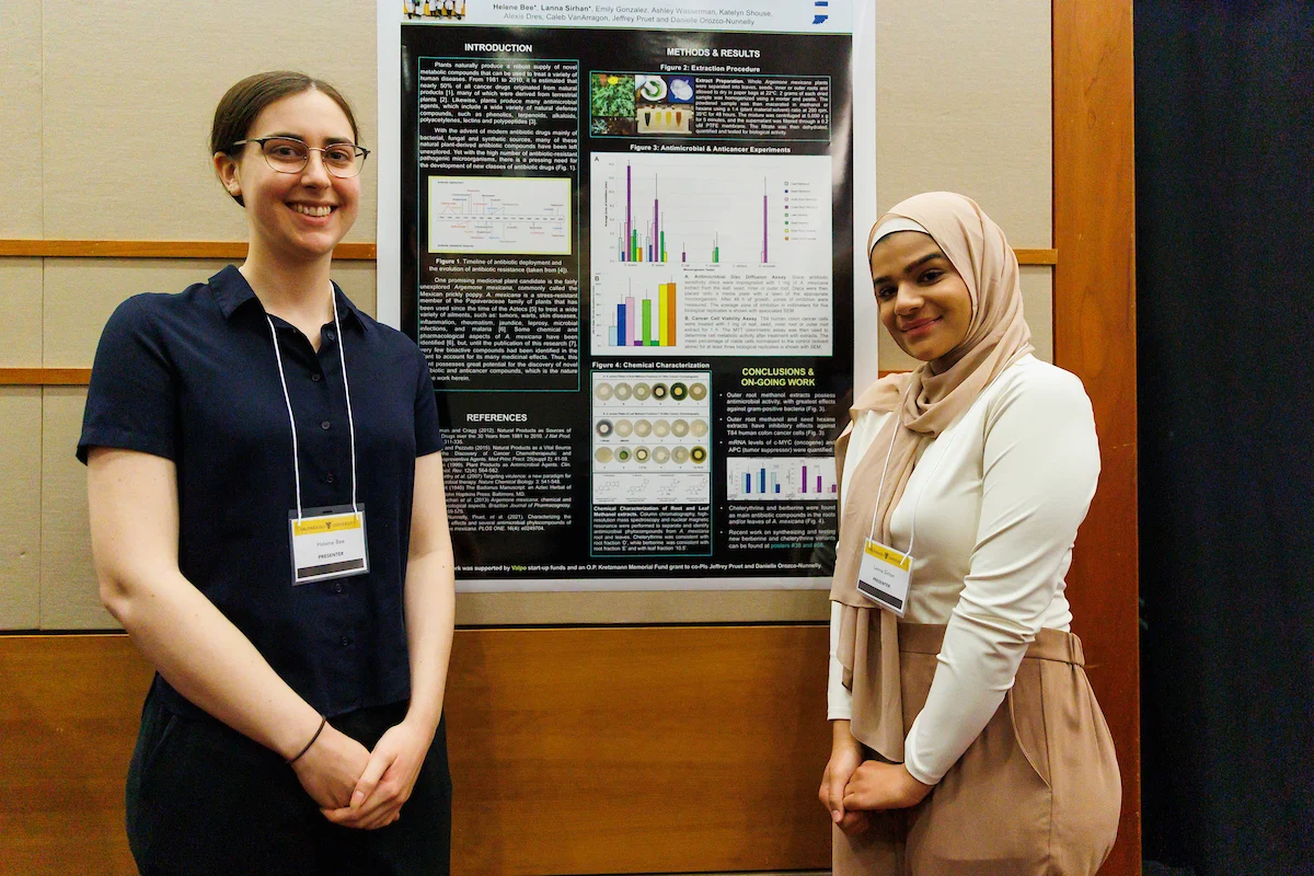 Two women standing and smiling in front of a scientific research poster at the Symposium on Undergraduate Research and Creative Expression.