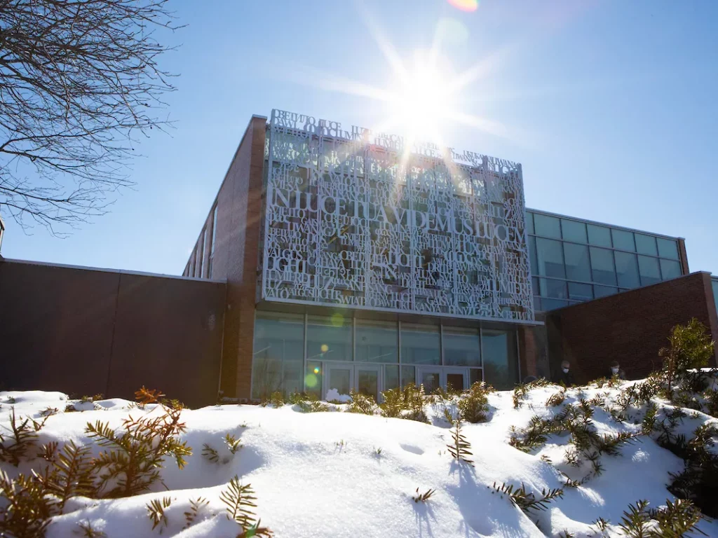 A modern building with decorative metalwork, sunlight shining above, and snow covering the ground in front—ideal for students pursuing Criminology or a Criminal Justice program.